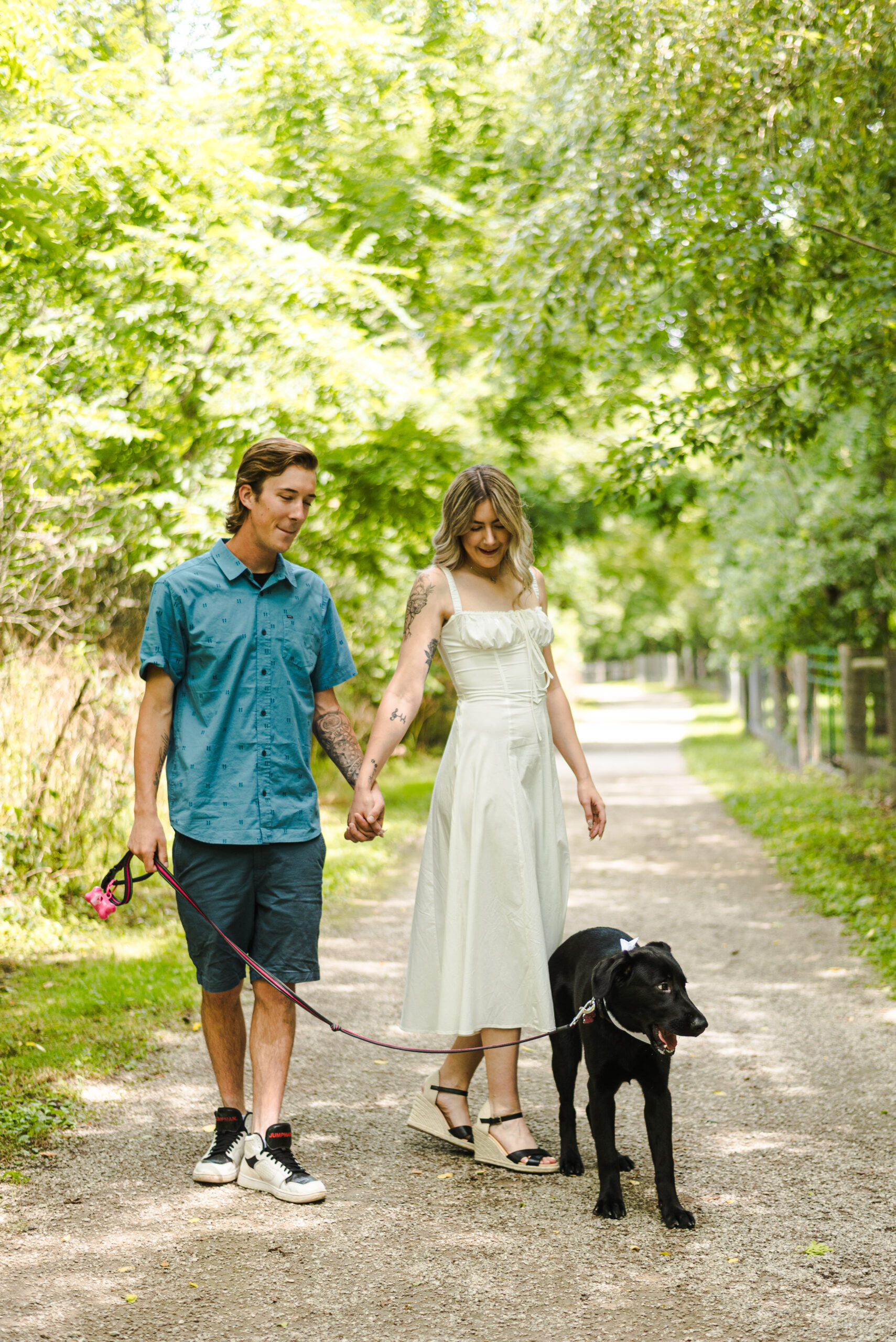 couple walking down a tree lined trail with their puppy during their engagement photoshoot in ontario, canada.